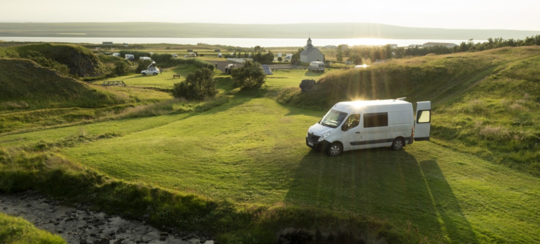 Een buscamper geparkeerd op een grote groene camping in IJsland met prachtig uitzicht