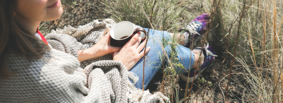 Vrouw drinkt kopje koffie in het gras onderweg met de camper