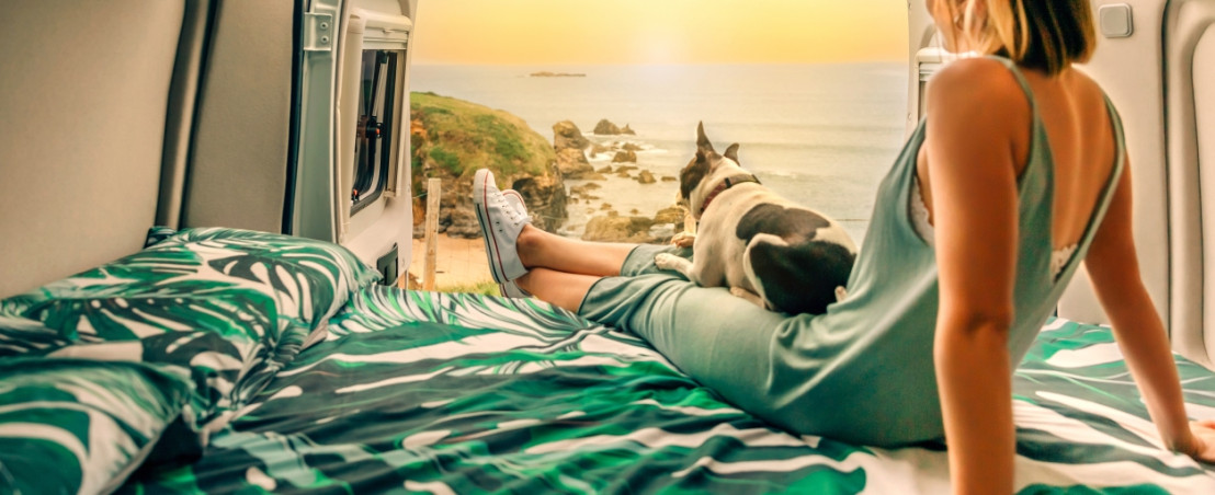 Vrouw geniet van uitzicht vanuit camperbed met hondje erbij