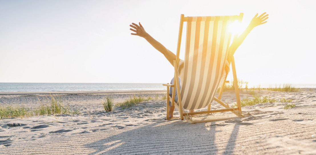 Vrouw zit in strandstoel op het strand en laat met haar handen zien dat ze zich vrij voelt