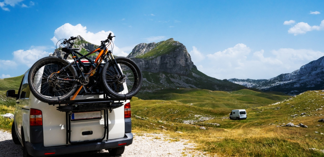 Camper met fietsen achterop op een plek met fantastisch uitzicht op de bergen