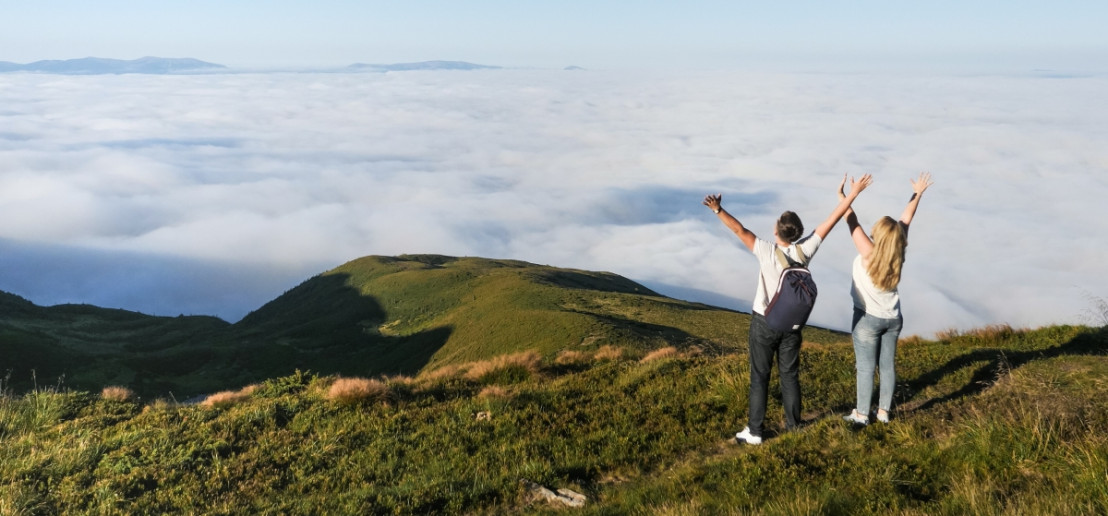 Jong stel gaat voor avontuur en staat op de top van de berg omringd door een prachtig uitzicht en wolkendek