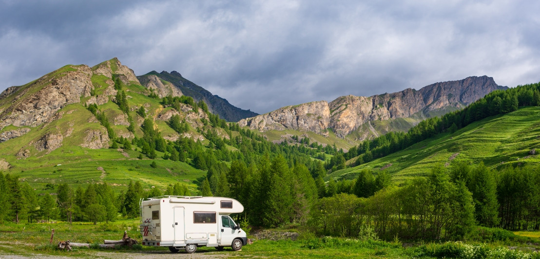 Camper staat geparkeerd in een omgeving met veel bergen, groen gras en een blauwe lucht