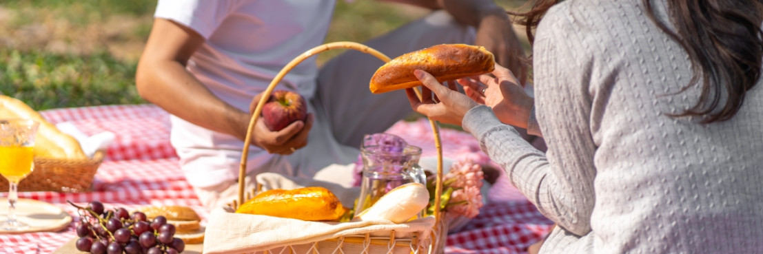 Een stel picknickt met verse broodjes en fruit op een kleed tijdens camperreis door rivierenland.