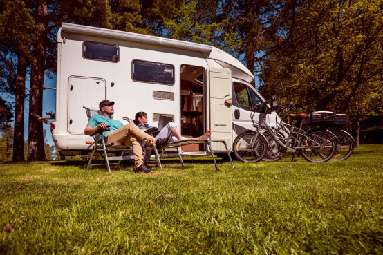 Stel is op reis met een gehuurde camper en zitten samen voor hun camper op een grasveld