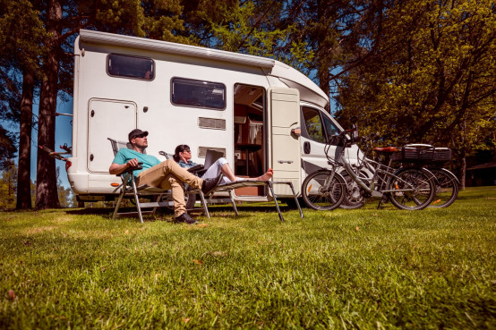 Stel zit voor de camper die geparkeerd staat op een veld met bos op de achtergrond